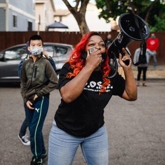 A black woman with red hair with Bay Rising holding a megaphone