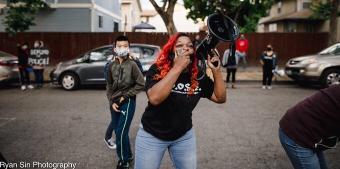 A black woman with red hair with Bay Rising holding a megaphone