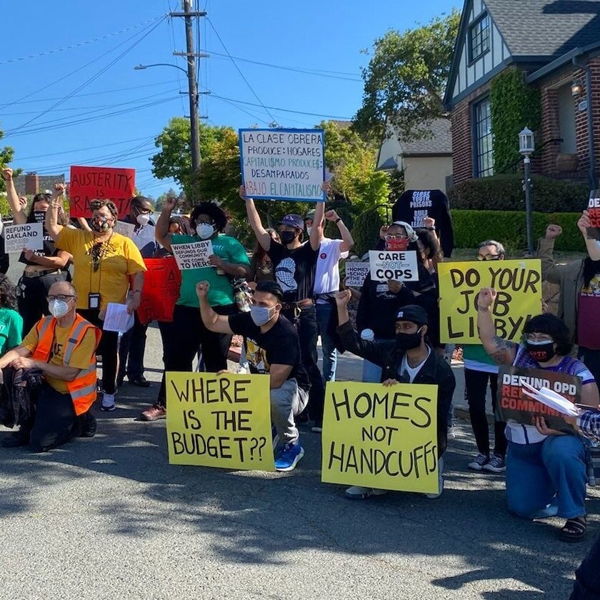 A large group of energetic people hold handmade poster board signs for Oakland Rising.