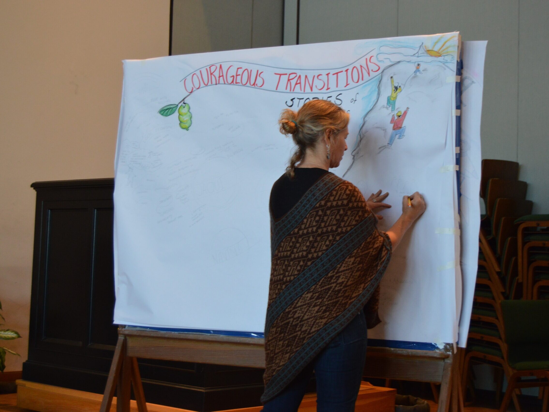 A woman drawing on a large canvas that says 'Courageous Transitions' at Beloved Communities Network