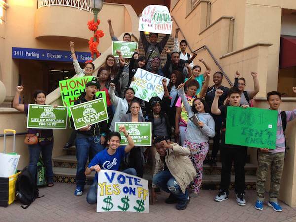 Young activists hold their fists in the air while holding a variety of poster board signs.