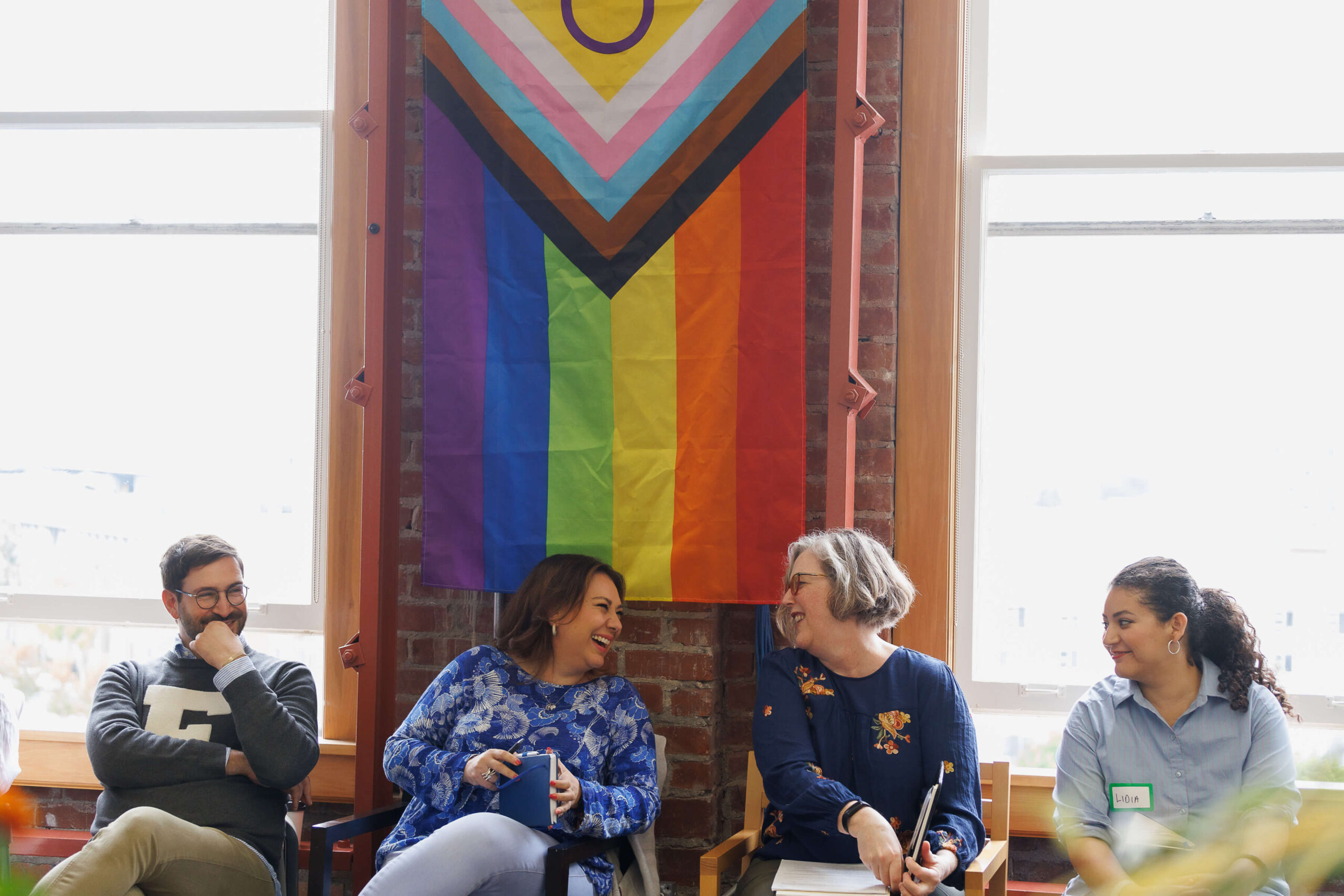MSC's staffers sit in front of a brick wall with large windows and a pride flag hanging on it