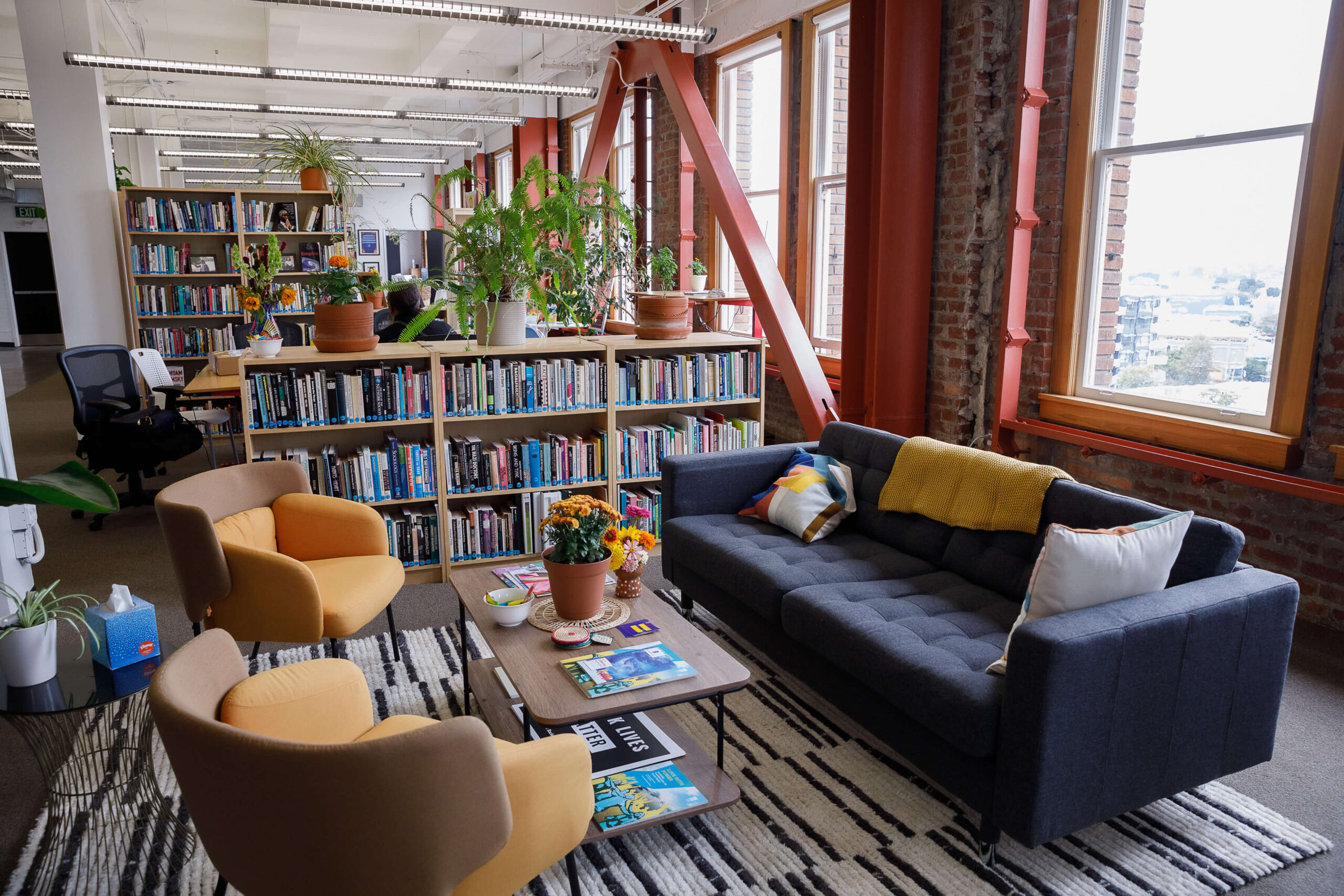 A blue couch and two yellow arm chairs surround a coffee table with bookshelves and a large open floor plan behind.
